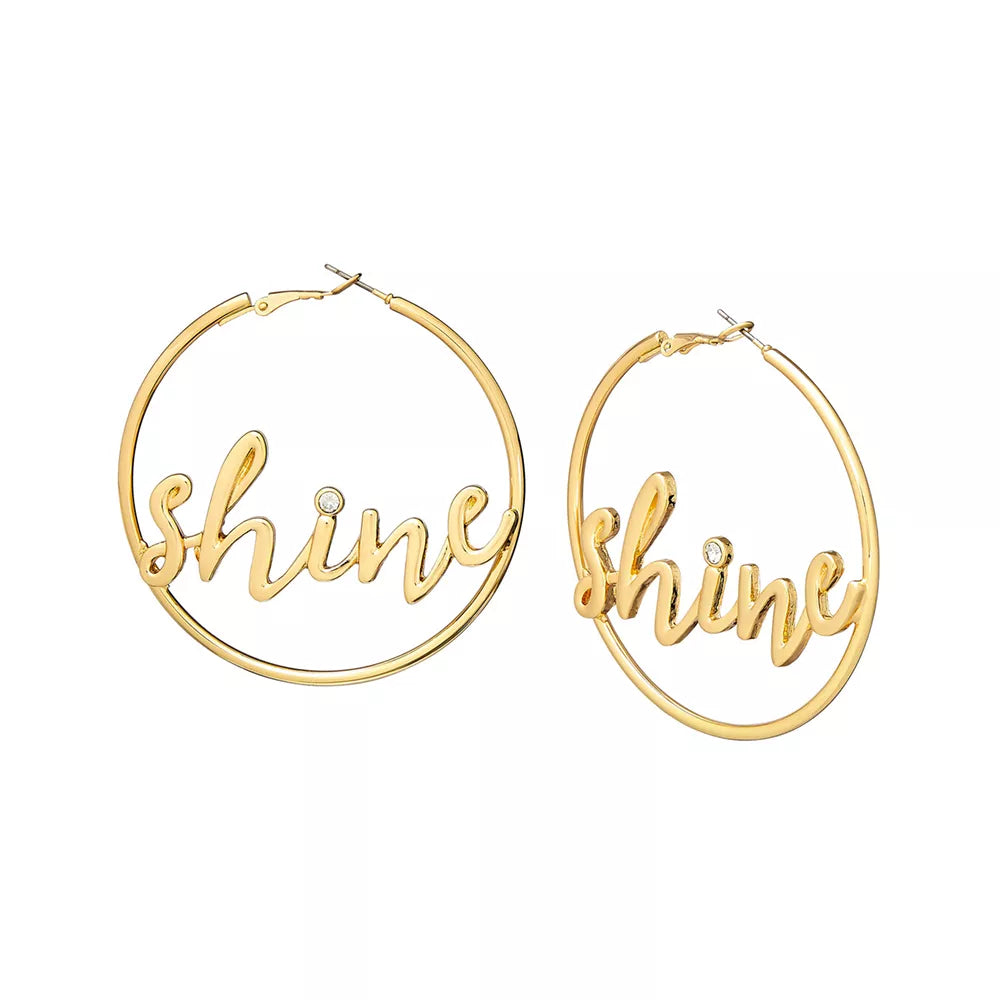 JE730_main "A pair of gold hoop earrings that are designed with the word "shine" in a cursive font. The earrings are displayed on a white packaging card labeled "arria by KISS." The card also indicates that the earrings are made of lead and nickel-free ma