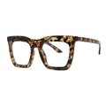 SUN16V5_main "A pair of stylish tortoiseshell glasses resting on a white, wavy-edged dish. Next to the glasses is a small tube of cream or lotion, which has a reddish-brown color and a sleek design. The background consists of light wooden planks, creating