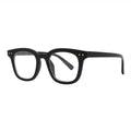 SUN20V5_main "A pair of stylish eyeglasses with a bold, black frame. The design is characterized by a square shape with slightly rounded edges, giving it a modern and sophisticated look. The glasses have clear lenses and are adorned with two small gold do