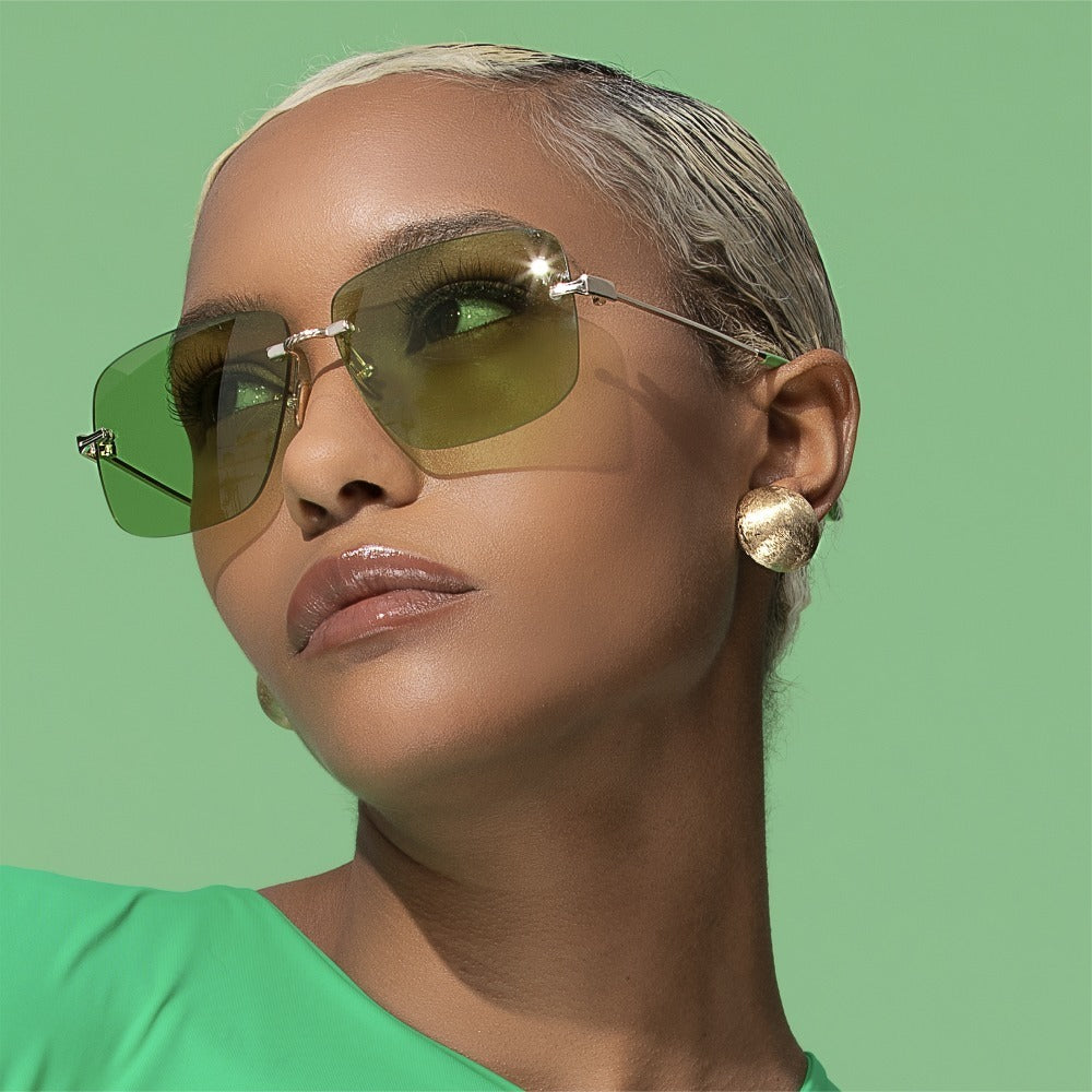 SUN48V2_main "A pair of rimless sunglasses with green-tinted lenses. The lenses are rectangular in shape with slightly rounded edges. The bridge and temples of the sunglasses are metallic, with the temples having a green coating towards the ends. The nose